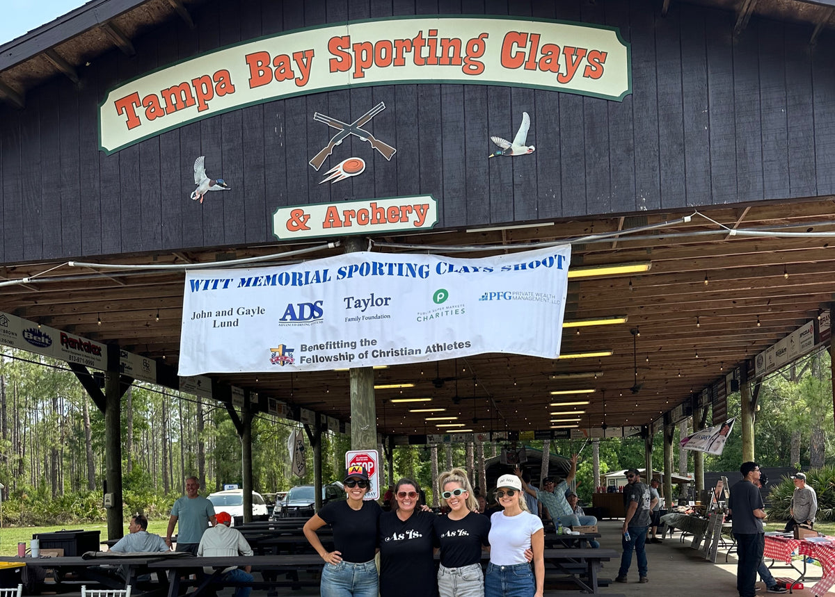 Group of people standing in front of a building with 'Tampa Bay Sporting Clays & Archery' sign.