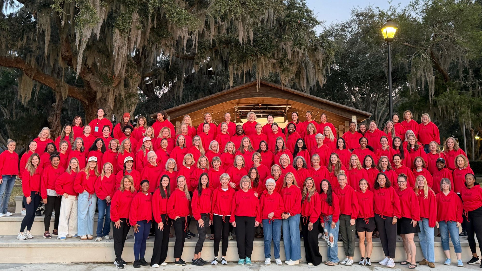 Large group of people wearing red hoodies gathered outdoors, community event and team unity