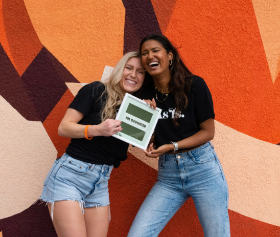 Two women smiling and posing in front of colorful mural, friendship and confidence