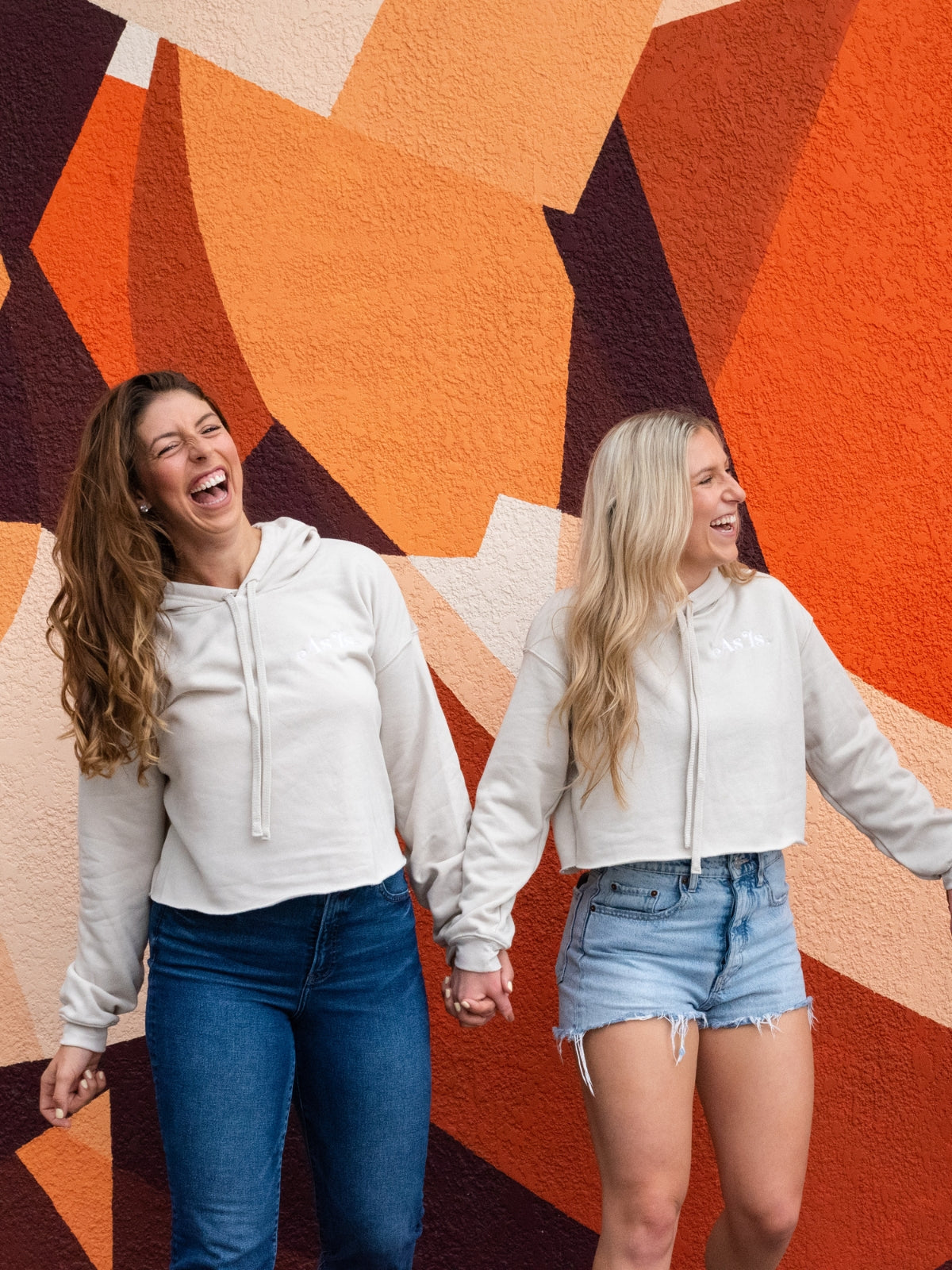 Two women dancing and smiling in front of geometric mural, joyful lifestyle